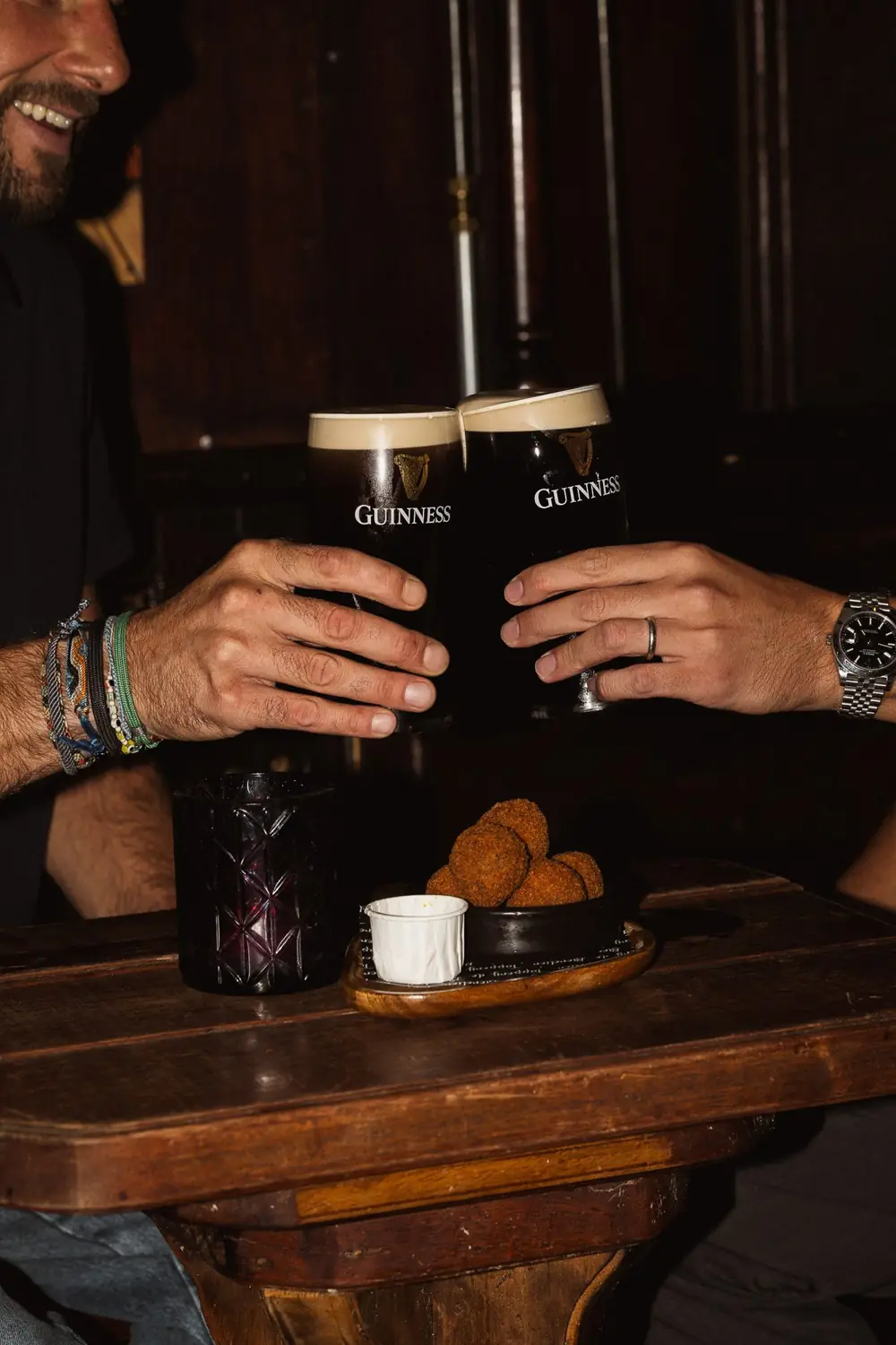 Twee volle Guinness proosten boven een schaal bitterballen